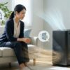 リビングで空気清浄機をいつ使うか考える日本人女性。24時間、電気代、メンテナンス、効果を視覚的に表現したアイキャッチ画像。