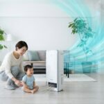 リビングで空気清浄機に見守られながら、澄み切った空気の中で笑顔を浮かべる日本人の親子。