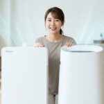 ダイキンとシャープの空気清浄機（左：ダイキン、右：シャープ）が並ぶ、清潔な日本人家庭のリビング。日本人女性が紹介している。