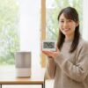 加湿器を片付けるタイミングを判断する日本人女性と湿度計。春の快適な室内環境を象徴。